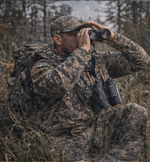 Man in camouflage gear using binoculars in a forest setting