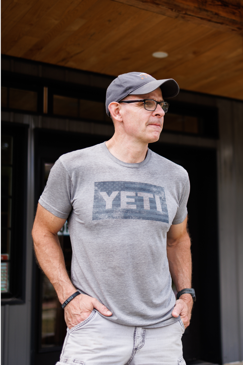 Man wearing a gray YETI t-shirt and cap standing outside a building.