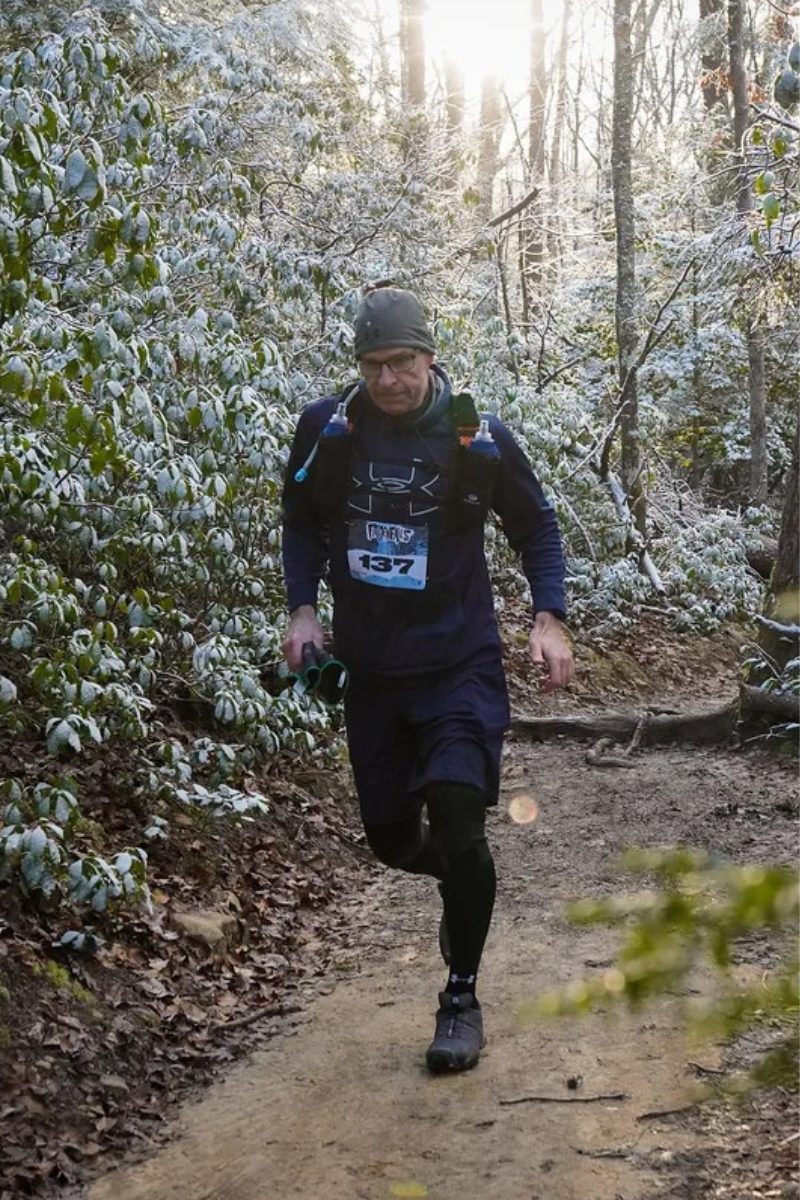Man running on a snowy forest trail wearing a race number