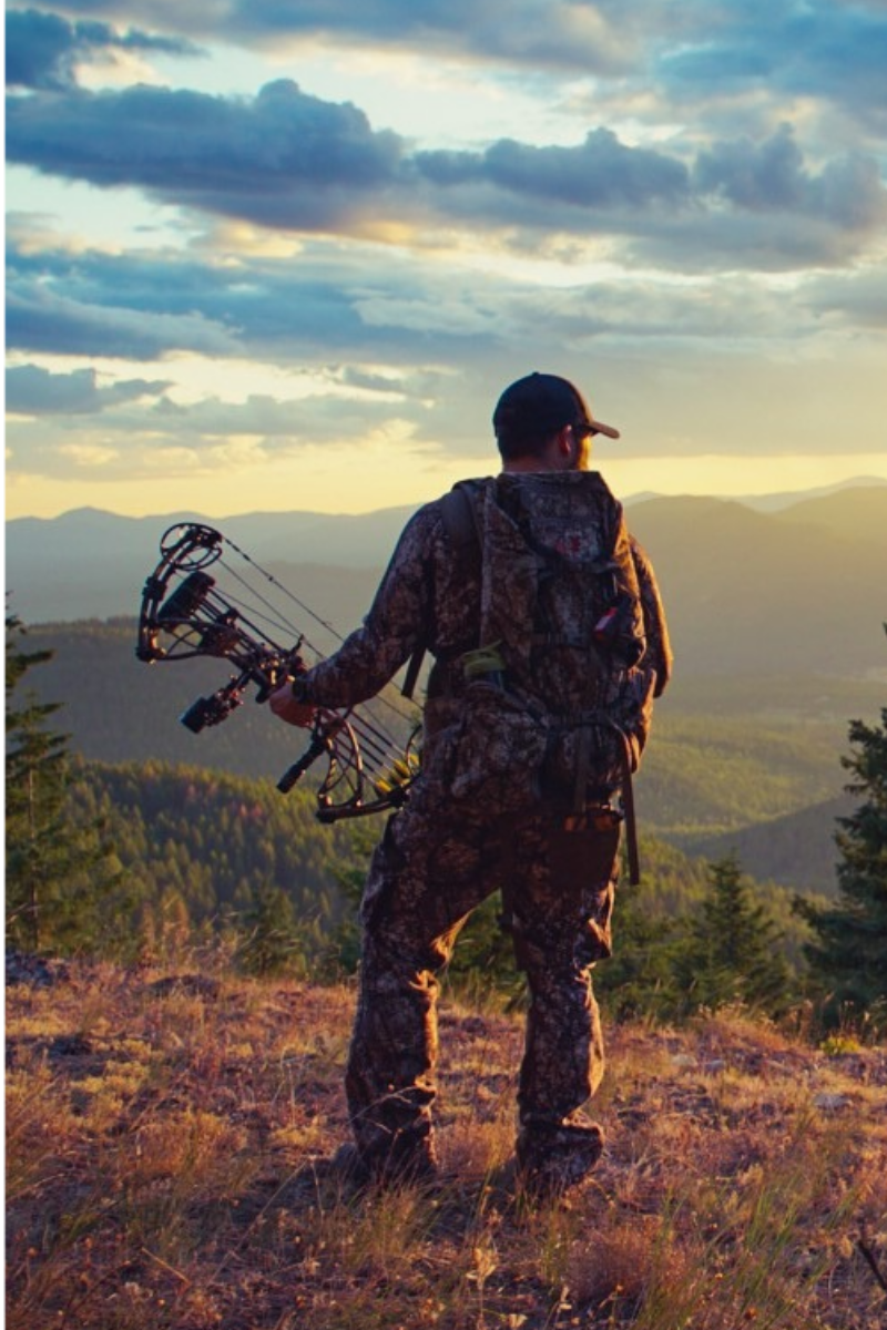 Hunter with bow standing on a mountain ridge at sunset